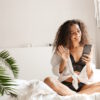 Image of woman wearing lingerie holding smartphone on bed in apa